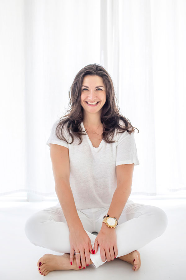 Amelia Pavlik sitting cross legged on floor with white outfit on in white room